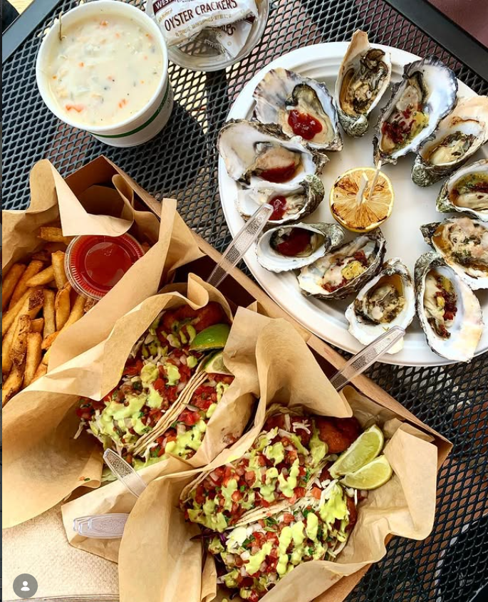 Clam chowder, BBQ oysters, fish tacos, and fries spread across a patio table