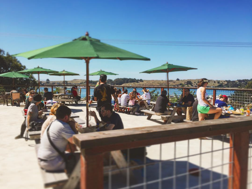 Guests on the bayside patio under green umbrellas