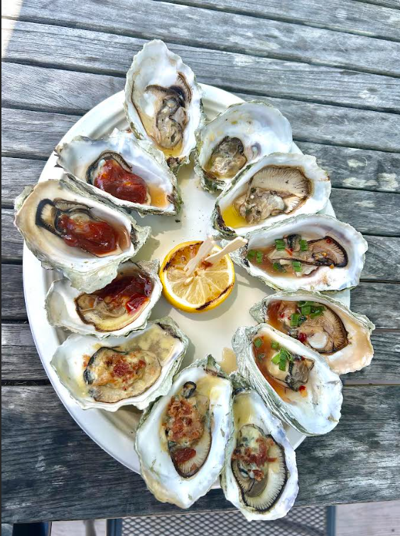Dozen BBQ Hog Island oysters arranged around a grilled lemon half on a white platter