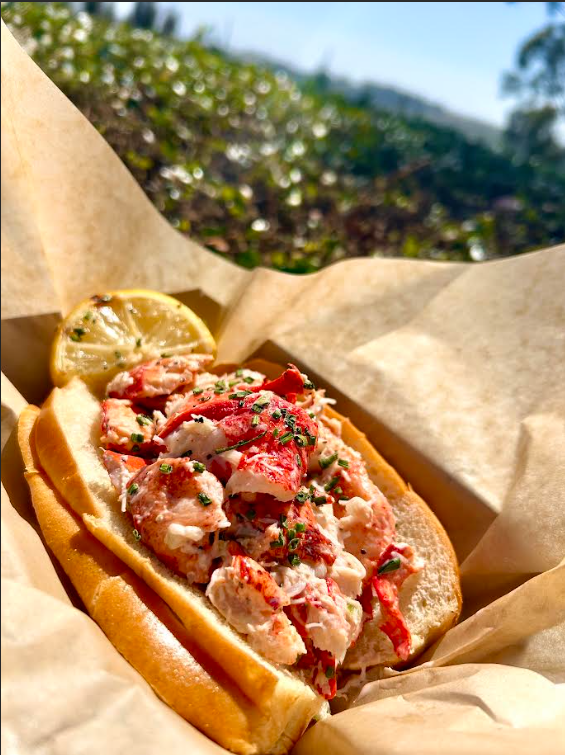 Buttered lobster roll topped with chives and a grilled lemon slice